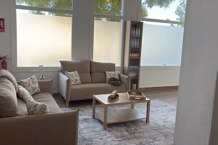 La sala de espera, con sofás claros, mesa de madera y alfombra